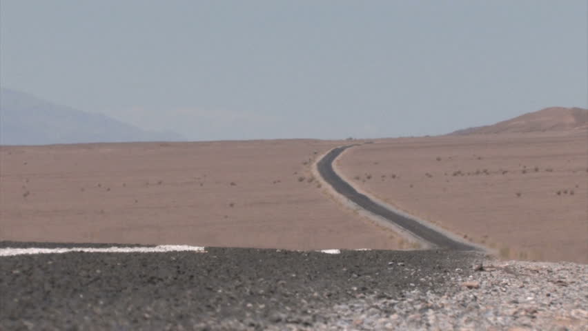 Car in the background on a Highway winding through the Desert with heat haze on