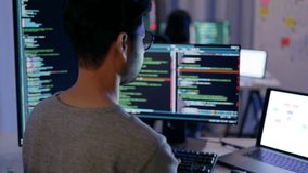 Rear view of a male programmer working on multiple monitors filled with code, highlighting a late work session in a high-tech environment. - Powered by Shutterstock - Get 15% off with code: PIKWIZARD15