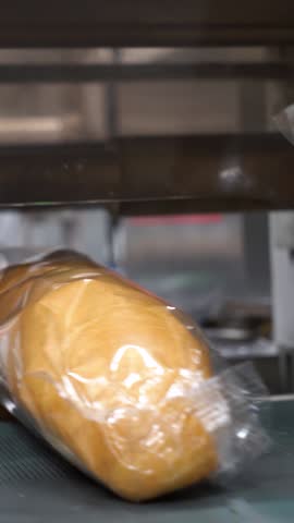 Fresh Bread Being Wrapped in Clear Packaging Film at Bread Packaging Line. Food Hygiene and Safety.  Bakery Worker Works on Bread Packaging Line. Bread Factory Production Line.