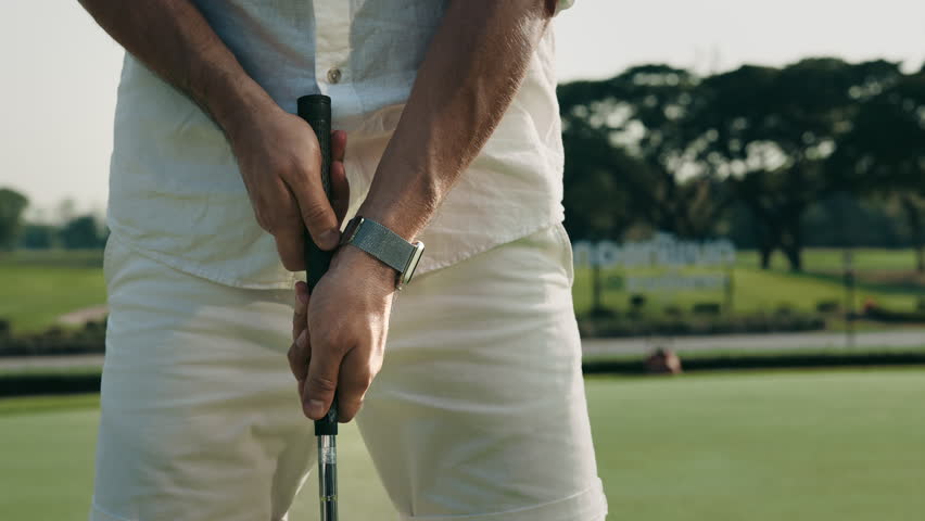 Player takes driver with both hands preparing to hit on course grass closeup. Professional golfer in white attire plays at golf tournament. Rich male enjoys sports game activity