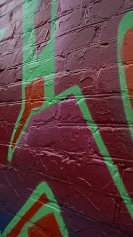 No people vertical closeup of freshly painted graffiti in bright purple, red, orange, acid green gradient colours on brick wall on city street at daytime