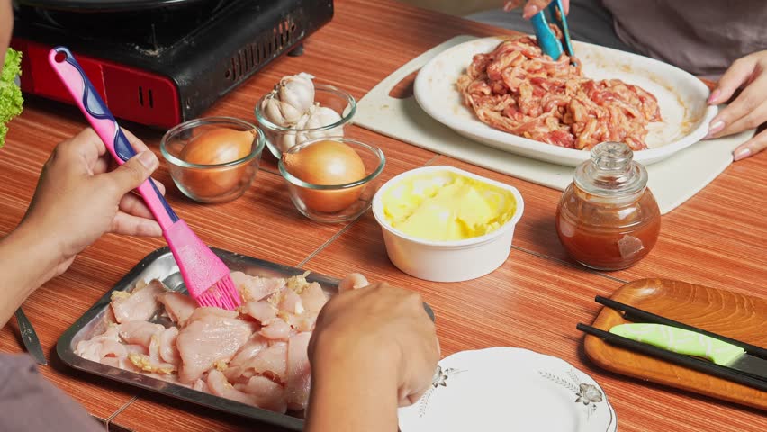 Asian Man And Woman Marinating Chicken Meat And Beef Slices With Spice For Making Korean Barbeque Style