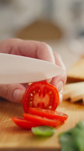 Vertical screen. Basil greens, Caucasian woman creates tomato sandwich on kitchen counter. Modern mother prepares Italian snack, applies new recipe for morning sandwich, rye bread

