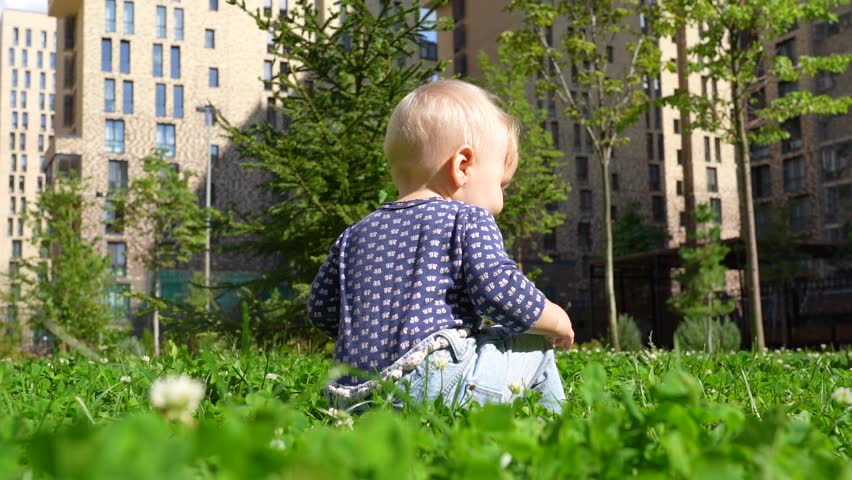 A baby crawls happily through the grass in a vibrant urban park