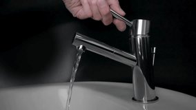 A close-up of a male hand gripping and turning a modern chrome faucet in a bathroom. Water begins to flow smoothly into a white porcelain sink, capturing a moment of daily routine. - Powered by Shutterstock - Get 15% off with code: PIKWIZARD15