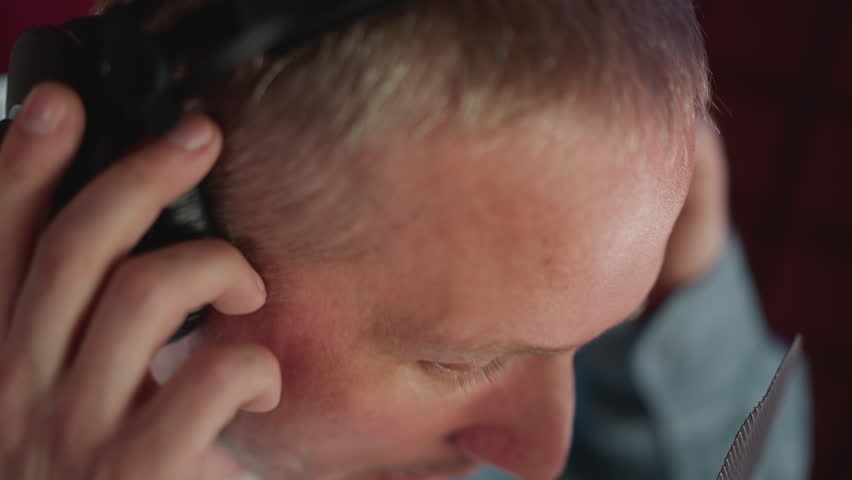 Close-up of a man wearing black studio headphones, with his hand adjusting them. ideal for themes related to music production, sound engineering, or podcast recording