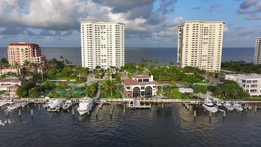 Yacht and boats at private pier with mansion and villas in background. Luxury apartment complex with ocean view on Boca Raton, Florida, USA. Aerial lateral wide shot.