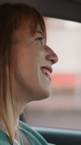 Happy woman smiles listening to music while driving car on city street. Positive female driver enjoys favorite song on way home closeup slow motion