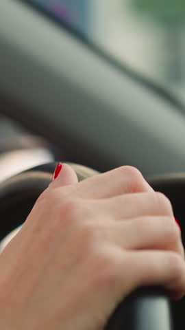 Woman turns steering wheel of car to sides moving fingers on blurred background. Female person with red nails enjoys driving vehicle closeup slow motion
