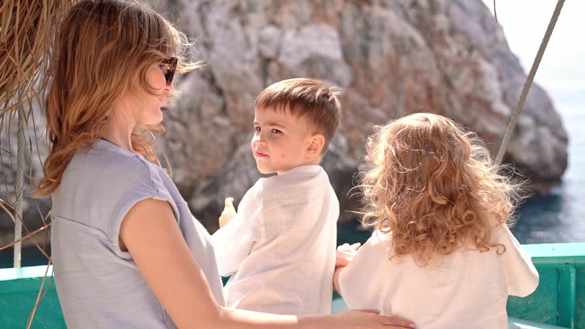 Mother with little son and daughter stands on board ship. They look at mountain they are passing by. Concept of travel, vacation and happy family.