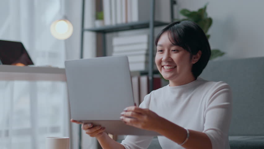 Young woman is working on her laptop computer at home and gets excited as she receives good news