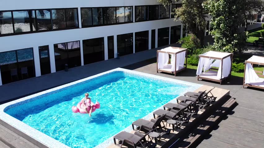 Aerial drone view of woman relaxing on flamingo pool float in pool in hotel. Summer holidays, enjoying summer vacations, luxury hotel