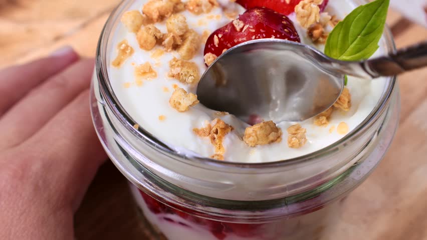 Eating homemade strawberry and yogurt parfait jar with fresh strawberries and granola with the spoon close up