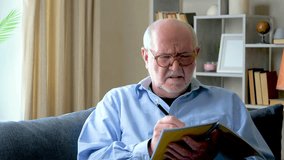 Elderly businessman man in blue shirt sitting on sofa at home doing work remotely checking financial report data. Slow motion. - Powered by Shutterstock - Get 15% off with code: PIKWIZARD15