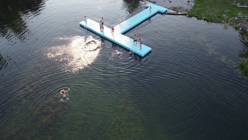 People having fun on the lake, aerial drone view. Children jump into the water. Tourists swim in the lake. Summer holidays. 