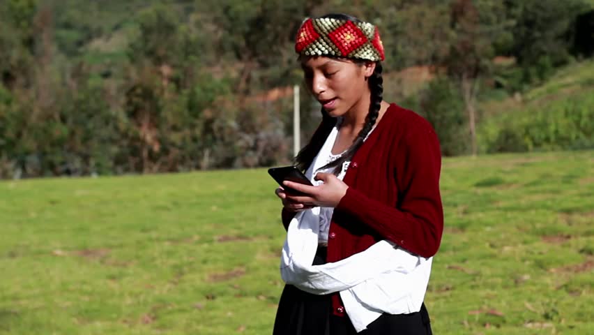 A happy Caucasian peasant woman talking on a smartphone wearing a hand-woven chopa. Peasant woman with typical Peruvian handmade clothing on a sunset in the Peruvian Andes. Women