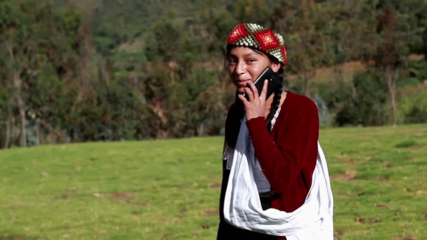 A happy Caucasian peasant woman talking on a smartphone wearing a hand-woven chopa. Peasant woman with typical Peruvian handmade clothing on a sunset in the Peruvian Andes. Women