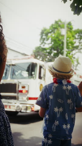 A young boy holds a mini US flag and waves at a passing truck, celebrating the fourth of July