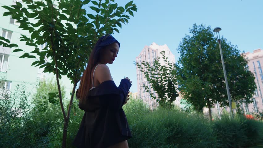 Young woman enjoying a drink in a sunlit urban park surrounded by greenery in the afternoon