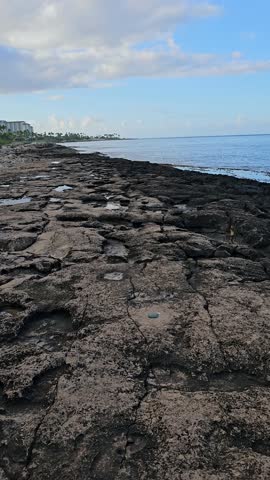 POV footage along the lava rocks on the beach with ocean water, waves, palm trees, hotels, blue sky and clouds on the island of Oahu at the Ko Olina Resort in Kapolei Hawaii USA