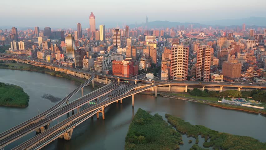 Aerial view at sunset above Zhongxing Bridge over Tamsui River with the crowded buildings in Ximending area bathed in warm sunlight and 101 Tower standing out in background, in Taipei City, Taiwan