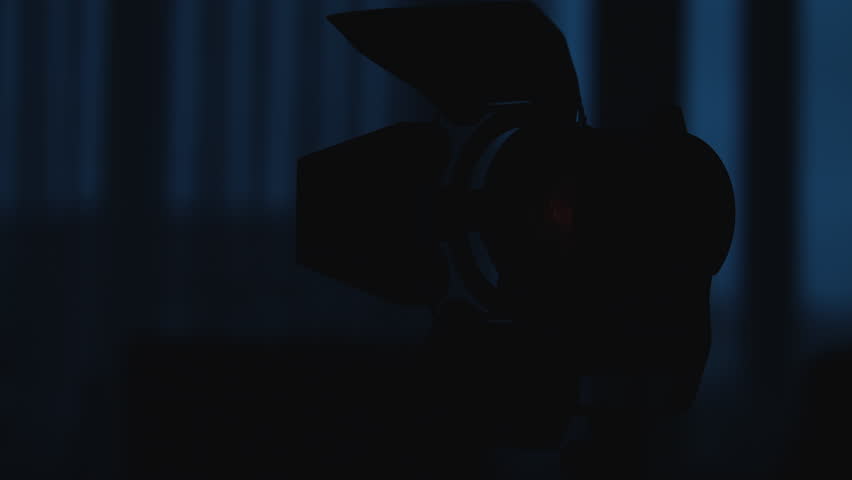Spotlight with Fresnel lens slowly turn turns on and off in front of black background.