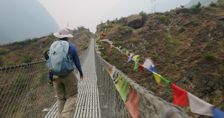 woman trekking on trail in nepal crosses suspension bridge