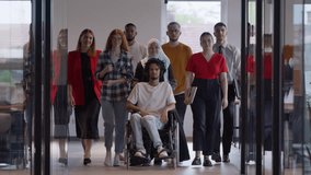 A diverse group of young business people congregates within a modern startup's glass-enclosed office, featuring inclusivity with a person in a wheelchair, an African American young man , and a hijab - Powered by Shutterstock - Get 15% off with code: PIKWIZARD15