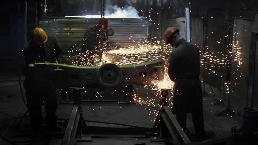 Workers are using grinders to work on a steel product at the metallurgy facility. Grinder tools are pushed against the product at metallurgy factory. Grinders smoothing the item at metallurgy factory.