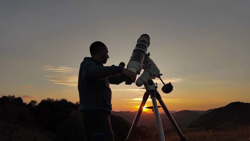 Amateur astronomer looking at the evening skies, observing planets, stars, Moon and other celestial objects with a telescope just before sun down.	
