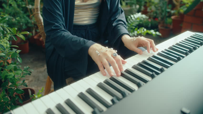 Woman with crystal-like embellishments on her hands playing musical keyboard during solo performance in greenhouse. Close-up shot