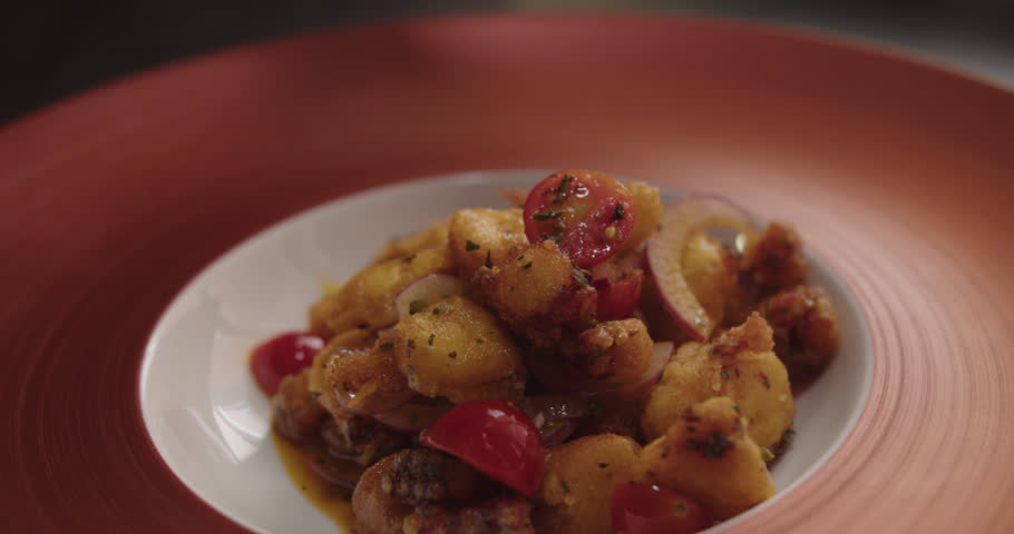 eautiful slow motion, close-up shot as the dish "octopus casserole" is served and presented with a spoon on a fancy plate inside a restaurant kitchen.