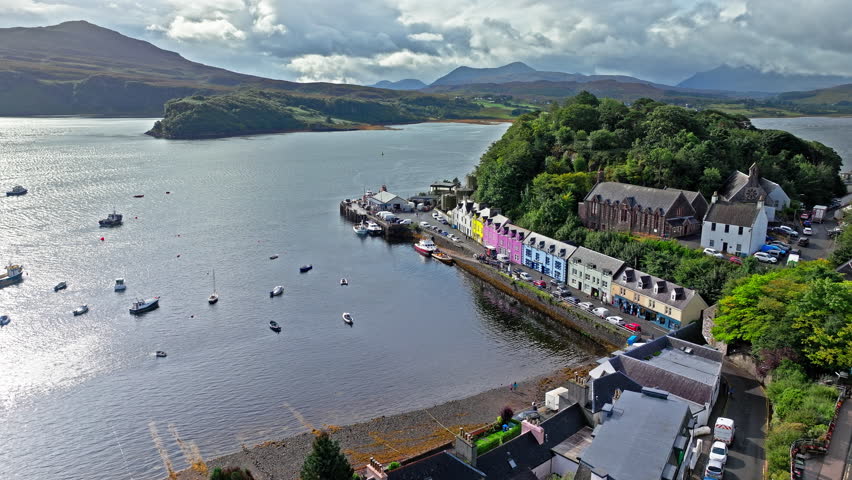 Aerial view of Portree town with colourful houses and fishing boats in Scotland. Scenic view of the natural harbour and port by high ground and cliffs. Popular tourist destination on the Isle of Skye.