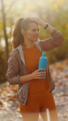 Hello autumn. stylish middle aged woman in fitness clothes in the park with bottle of water.