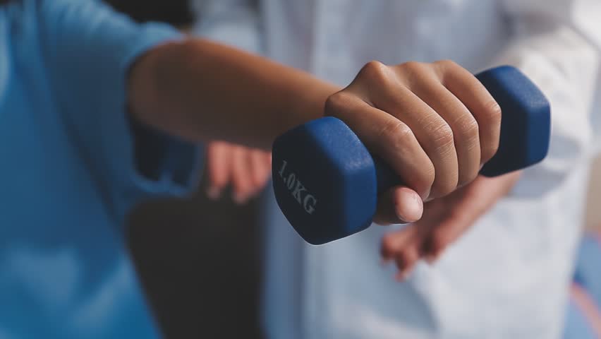 Young pretty asian physiotherapist helping senior female patient holding dumbbell in physical therapy session, concept of World Confederation for Physical Therapy.