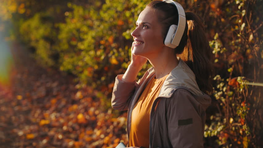 Hello autumn. happy modern woman in fitness clothes in the park listening to the music with headphones.