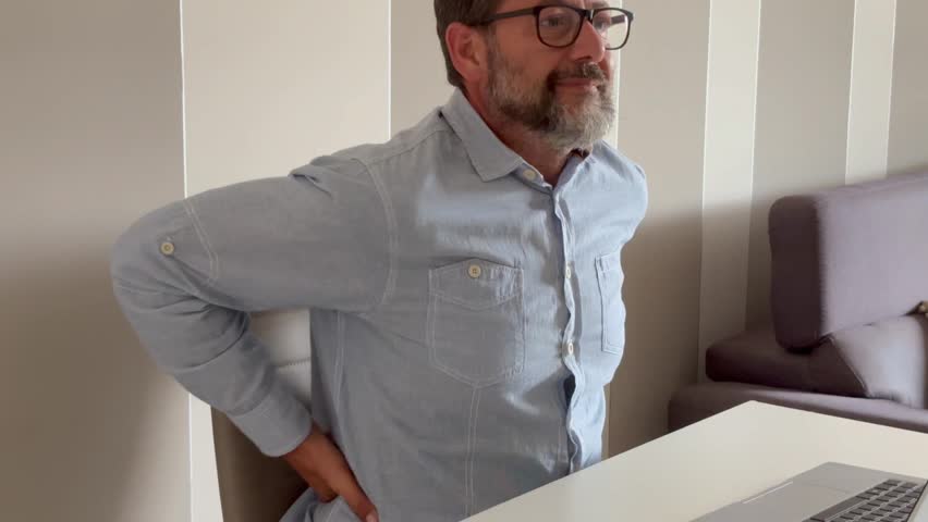 Adult man in glasses sit at table feels neck pain massaging tensed muscles after working on laptop overworking and sedentary lifestyle. Incorrect posture, chronic cervical ache, fibromyalgia concept