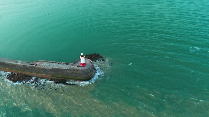 A phenomenal shot of the waves hitting the concrete cutwater. A lighthouse is rising on the edge of the cutwater.