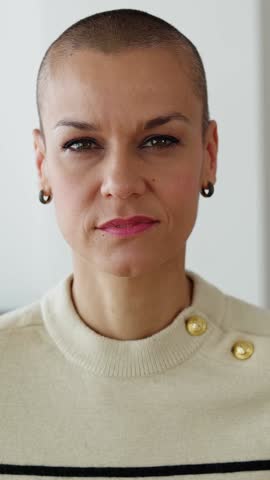 Vertical HD video. Mid adult woman with shaved head smiling at camera while standing at home. Happy people concept, headshot, video call, POV web conference, webcam.