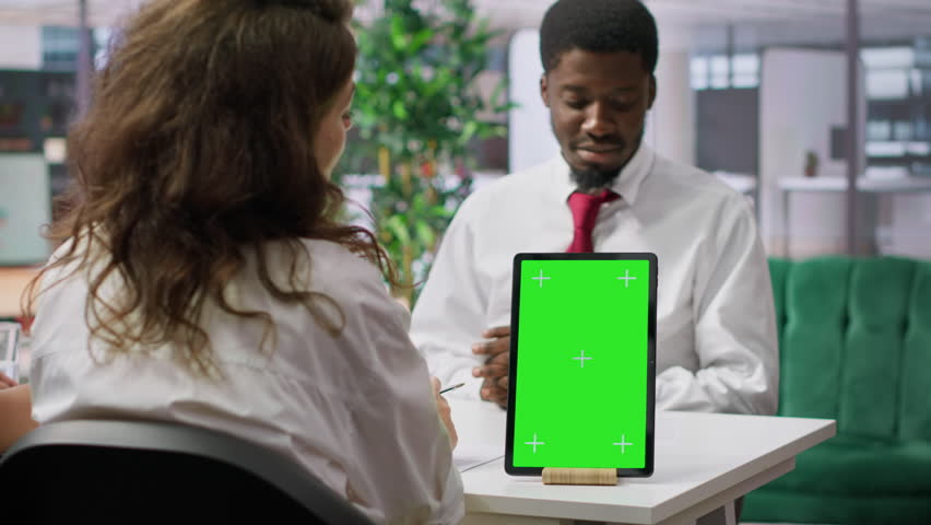 Job applicant and employer discussing in an interview with isolated mockup display on a device, high end corporate office. Businessman and HR recruiter share career development ideas. Camera A.
