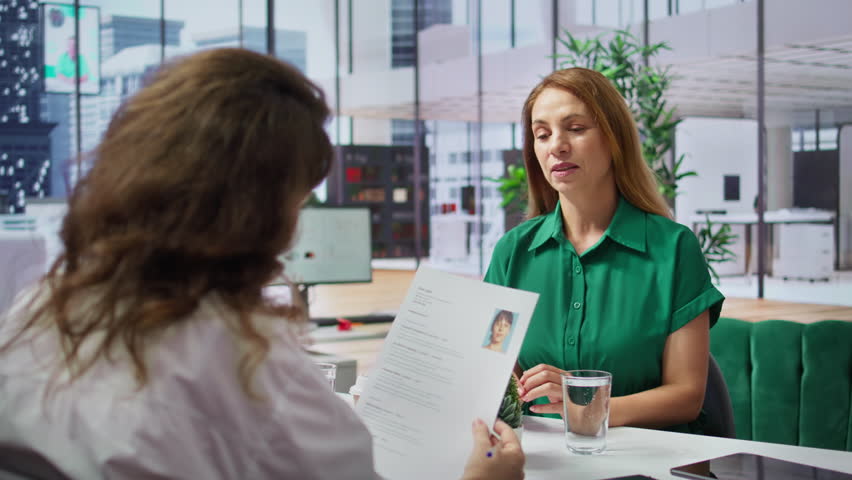 HR recruiter examines a candidate resume during a formal job interview, evaluating their qualifications during selection and recruitment process. Talent acquisition and recruiting. Camera B.