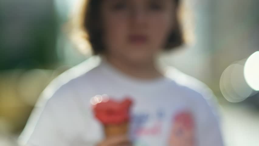 Teenage girl holds a melting pink ice cream in a waffle cone toward the camera, capturing a sweet and messy summer moment.