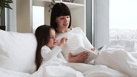 Mother reading bedtime story to young daughter in cozy bedroom with large window. Bonding moment between parent and child surrounded by peaceful atmosphere and warmth of home. - Powered by Shutterstock - Get 15% off with code: PIKWIZARD15