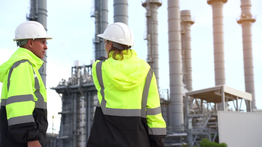 Team discussion about blueprint drawings inside Electricity Power Plant site. Senior Engineer wearing safety jacket and PPE working about Petro Chemical plant
