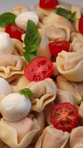 tortellini with mozzarella balls, cherry tomatoes, basil leaf, rotation in circle. fresh pasta, Turning. Typical Italian dish - ravioli tortellini stuffed with tomato sauce. Vertical video