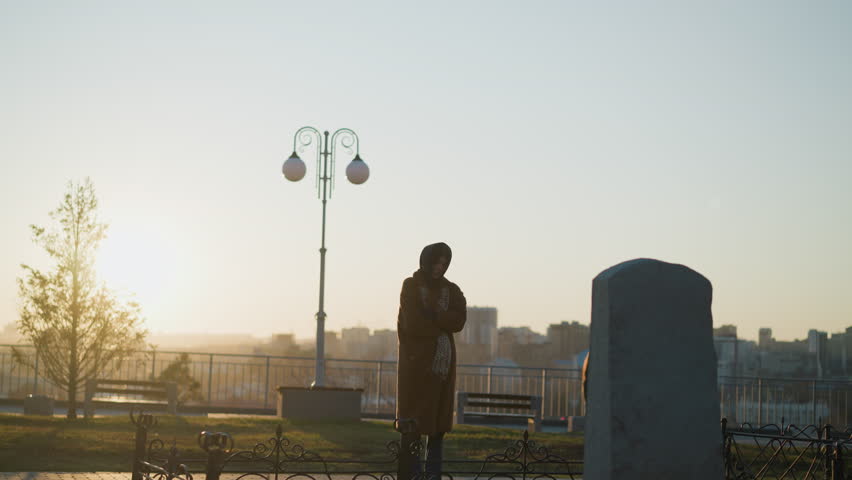 Tearful Woman Contemplating in Front of Stone Monument at Sunset in a Park