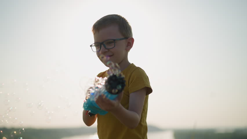 Young Boy in Yellow Shirt Smiling with Bubble Gun in Bright Sunlight