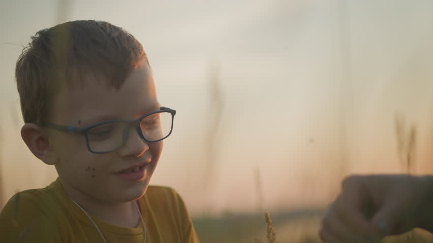 Young Boy in Glasses Smiling in a Serene Grassy Field at Sunset
