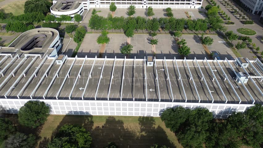Parking ramp to multilevel garage with rooftop angled parking layout, shade structure, traffic flow marking at lush green suburban campus building in Westlake, suburbs Dallas Fort Worth, flyover. USA