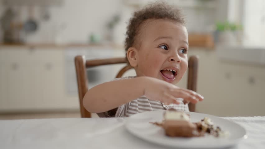 Family dinner, portrait of cute African toddler eating sweet cake with chocolate . Carefree childhood, infancy, enjoy delicious dessert, charming black little boy or girl licking fingers, funny face